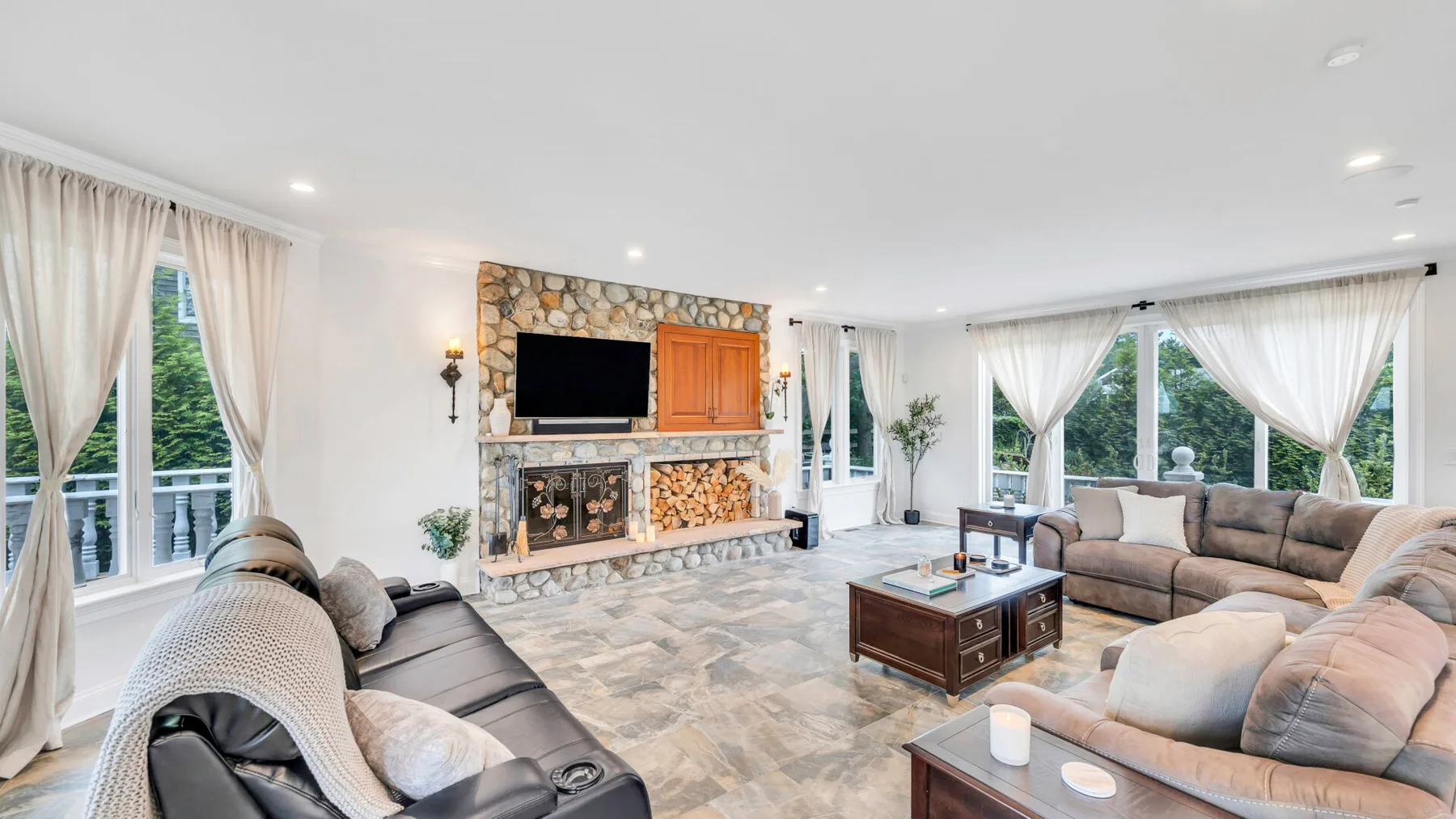 A living room with seating, a stone fireplace, and large windows.