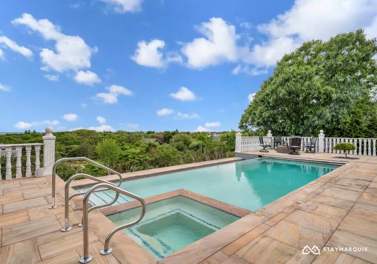 An outdoor swimming pool sits beside a paved deck and leafy trees.