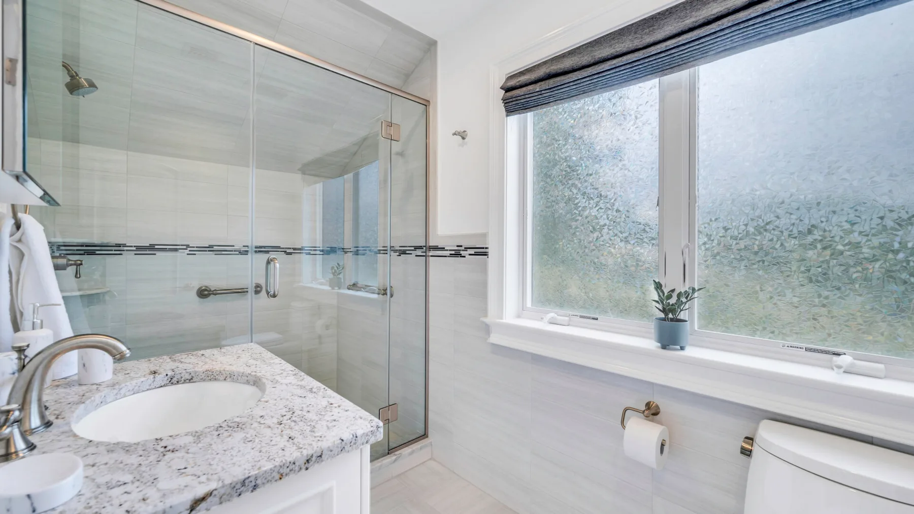 A bright bathroom with a glass shower, sink, and window.