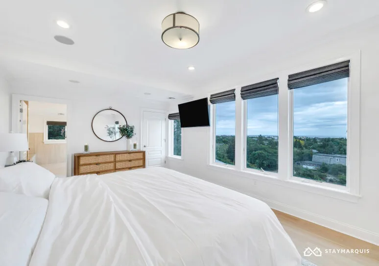 A bright bedroom with a large bed and wide windows overlooking greenery.