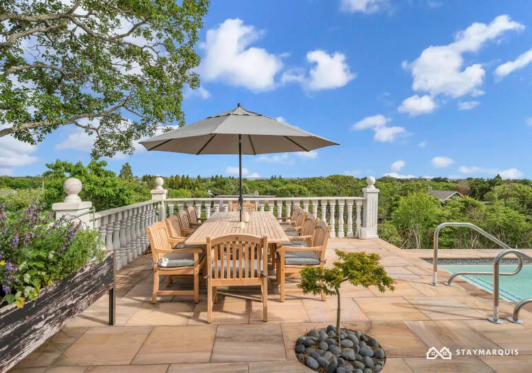 An outdoor terrace with a dining table beneath an umbrella and a swimming pool.