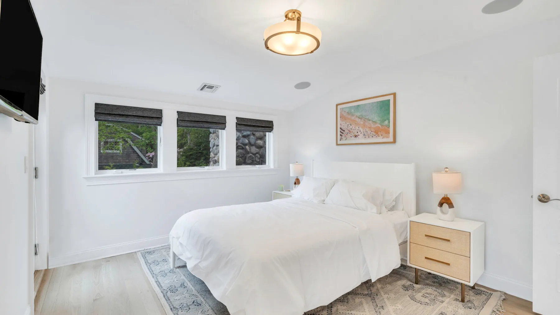 A bright bedroom with a neatly made bed and windows along the wall.
