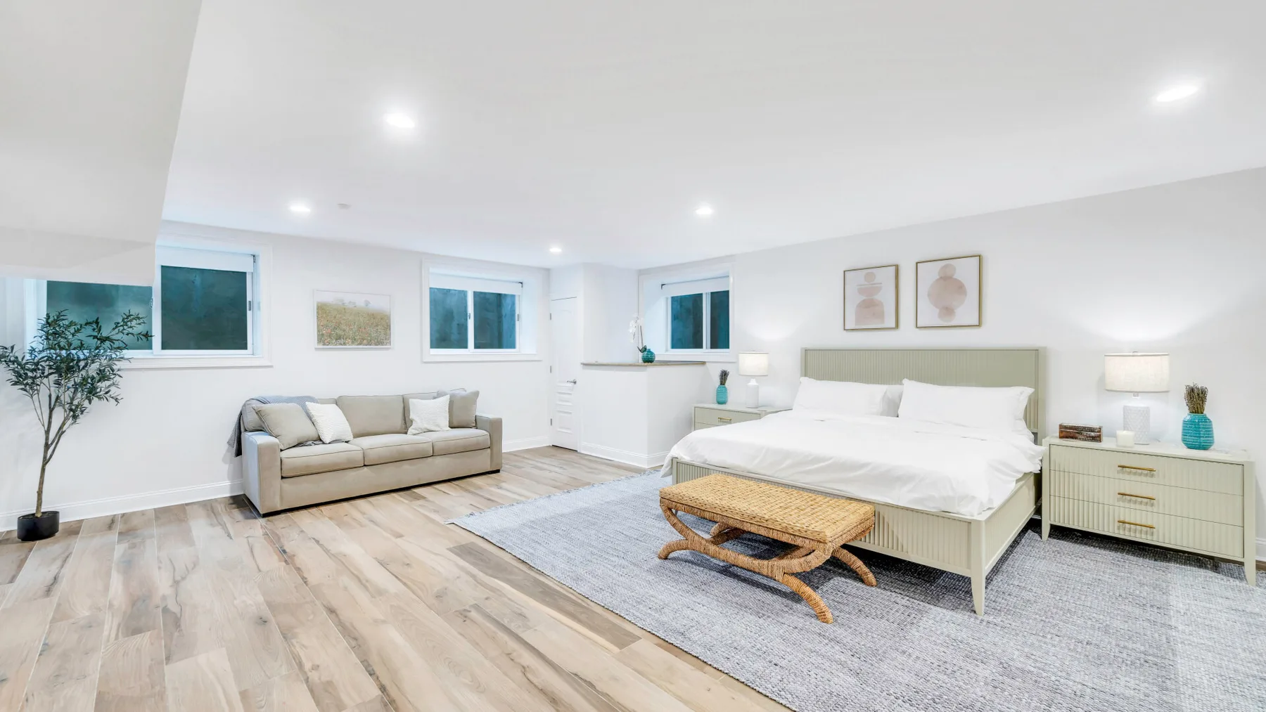 A bright bedroom with a large bed, a seating area, and windows.