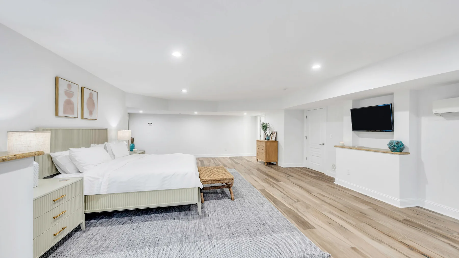 A bright bedroom with a bed, bedside furniture, and a wall-mounted television.