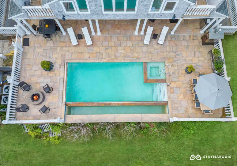 An outdoor swimming pool beside a paved patio with seating and an umbrella.