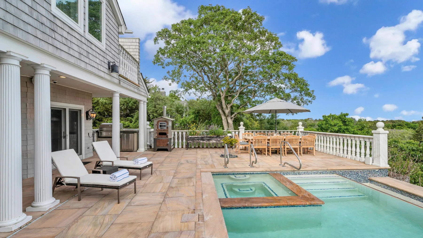 An outdoor pool beside a broad tiled patio with seating and a dining table.
