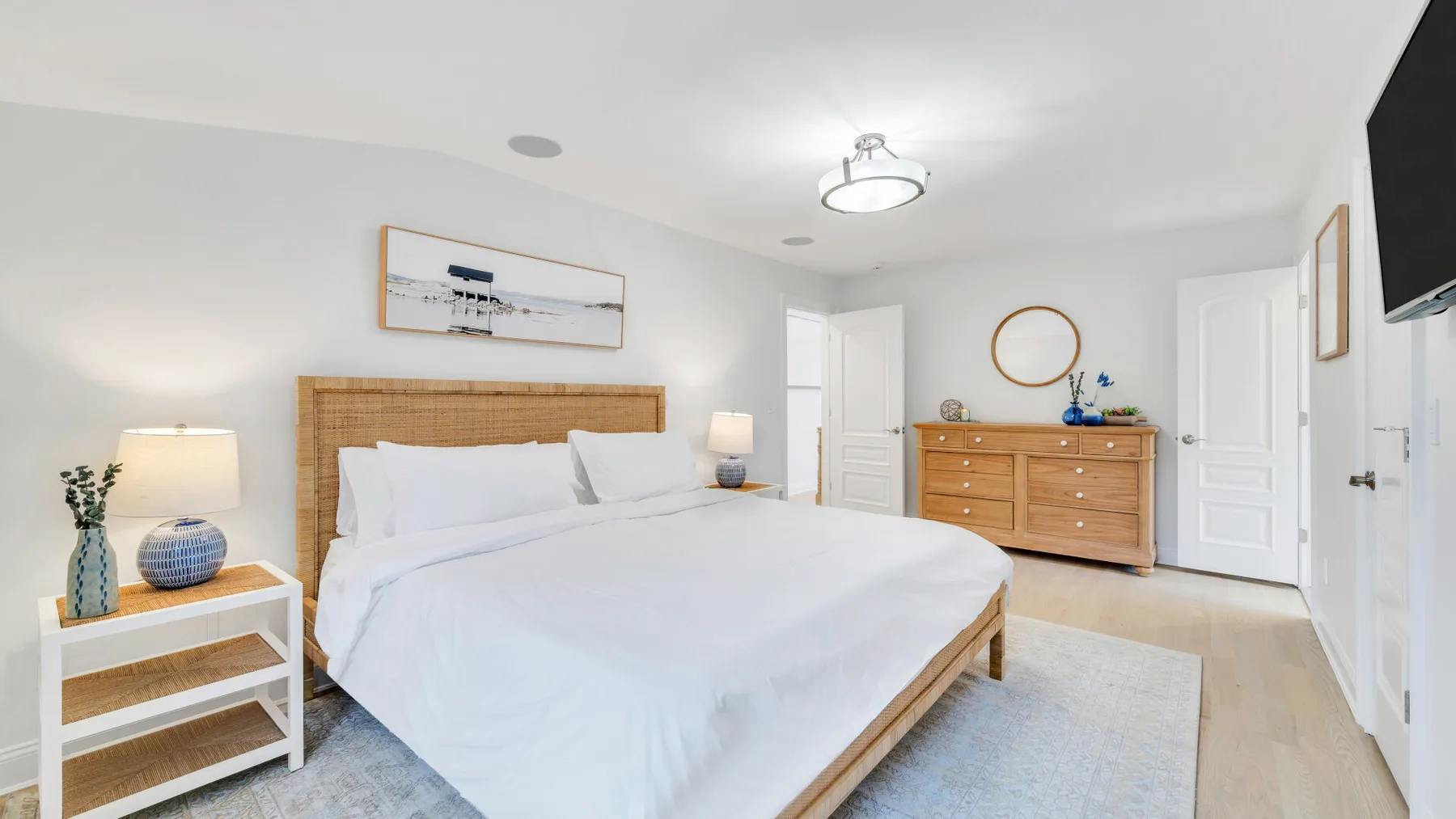 A bright bedroom with a neatly made bed and wooden dressers.