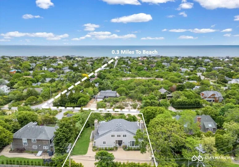 An aerial view of a coastal neighborhood with homes, greenery, and the ocean beyond.
