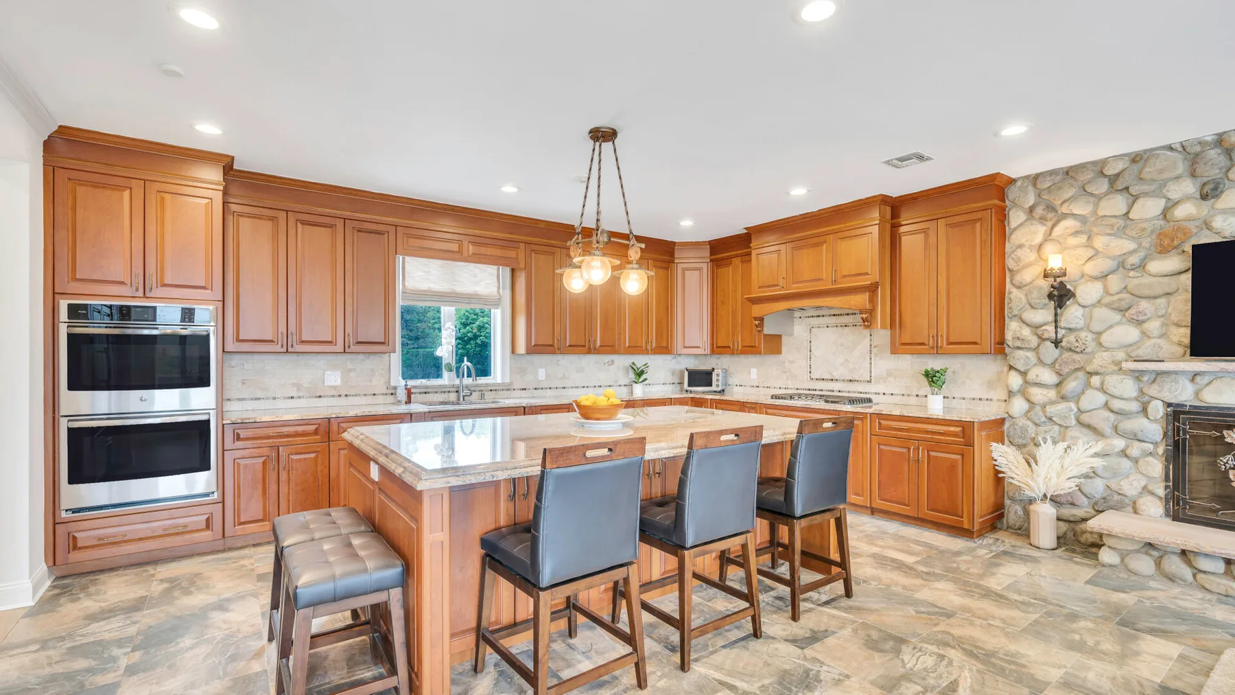 A spacious kitchen with wooden cabinetry, a large island, and a stone accent wall.