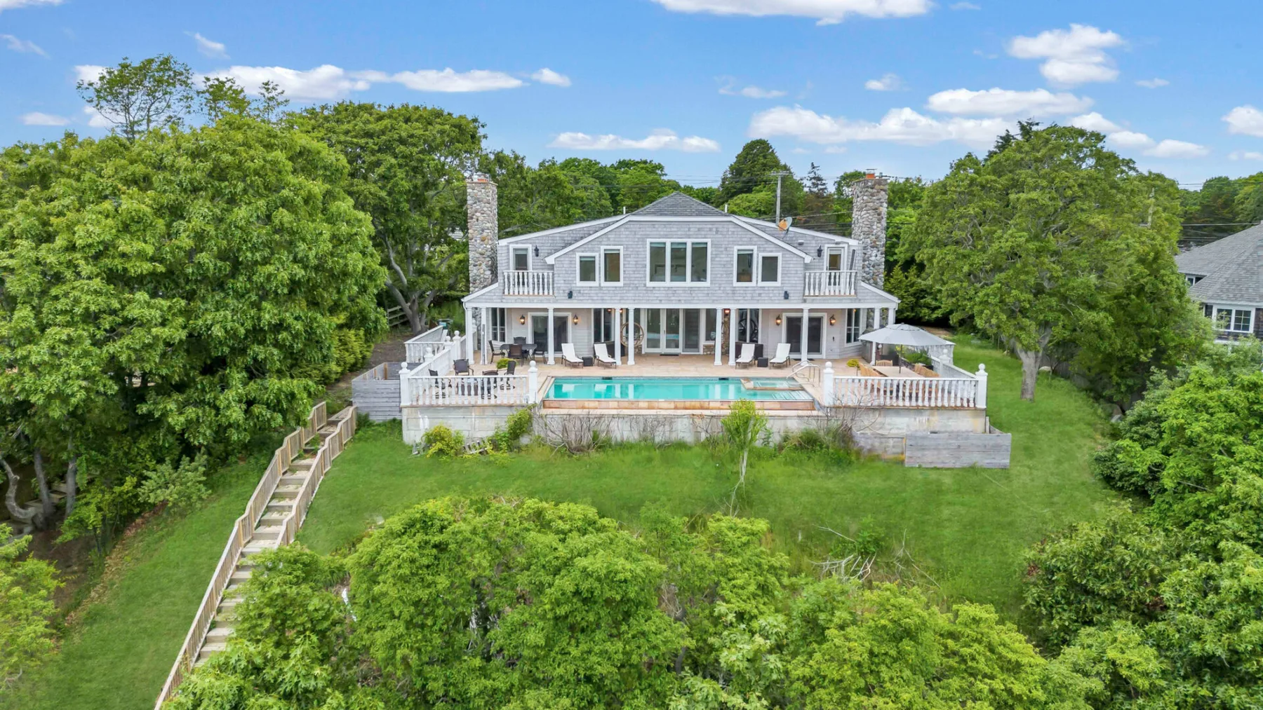 A large house with a swimming pool sits amid trees and green grounds.