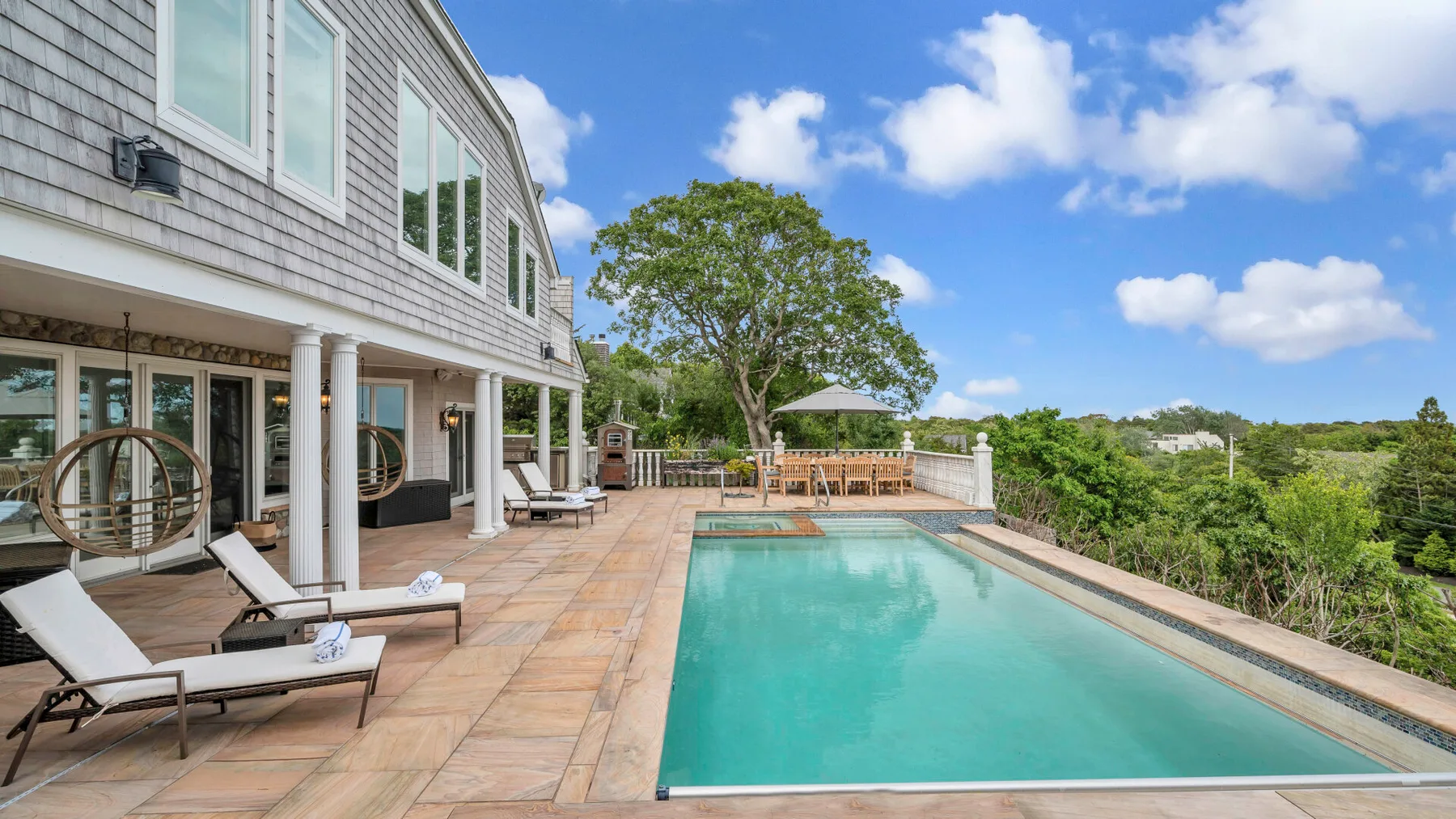 A swimming pool beside a house, with lounge seating on the paved patio.