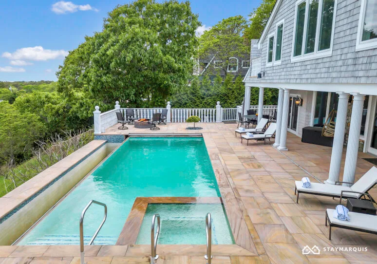 A swimming pool and paved patio beside a house, surrounded by trees.