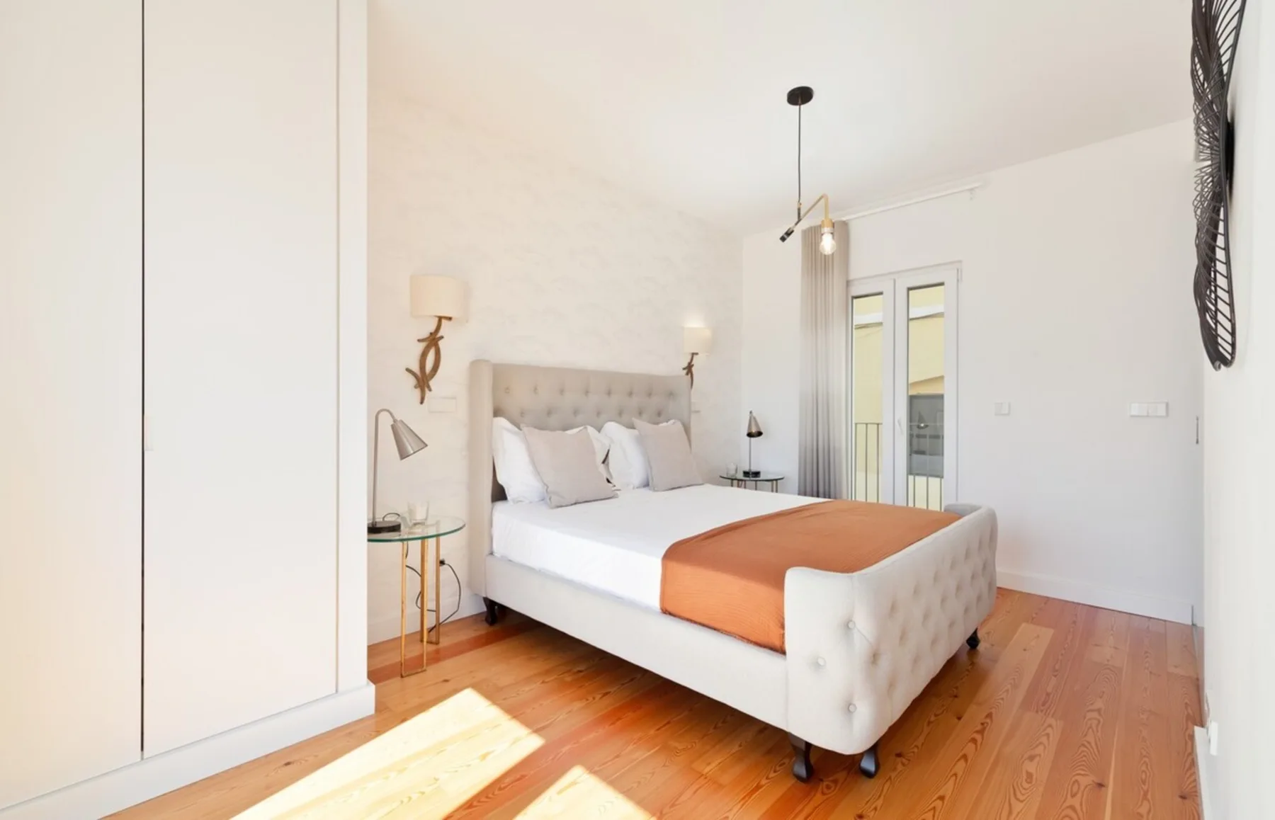 A bright bedroom with a tufted bed and orange bedspread.