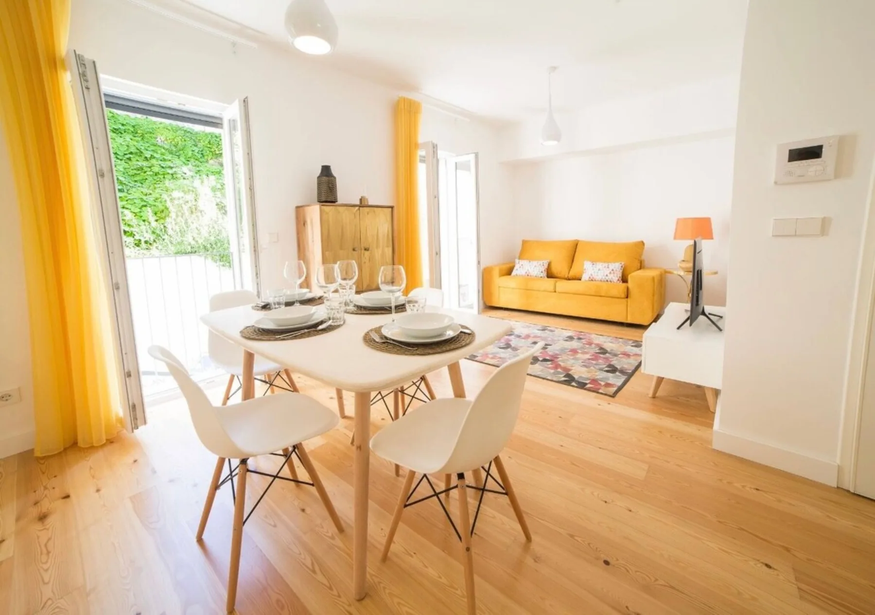 A dining area with a set table and a living area with a yellow sofa.