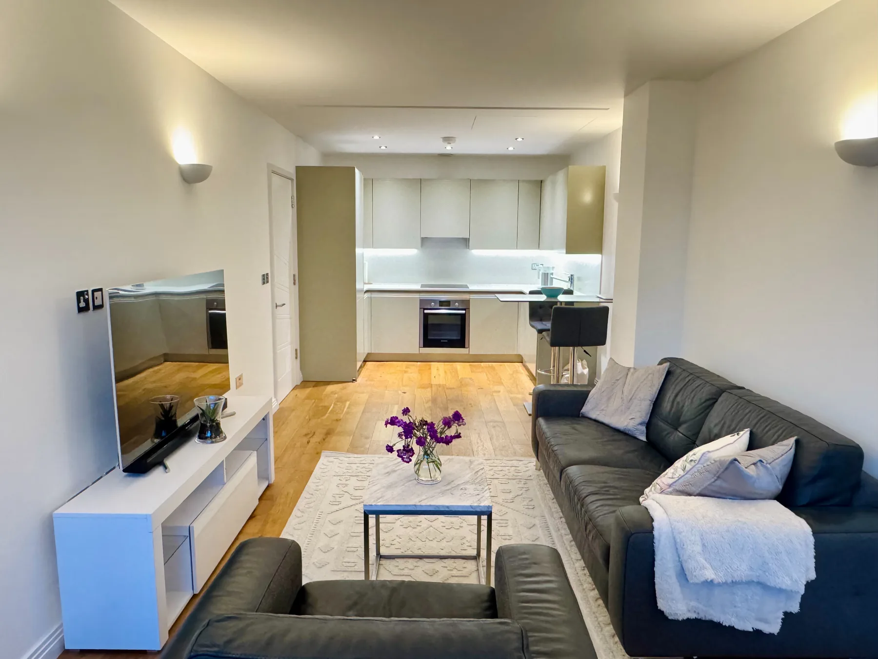 Una sala de estar con asientos y televisión, abierta a una cocina compacta.