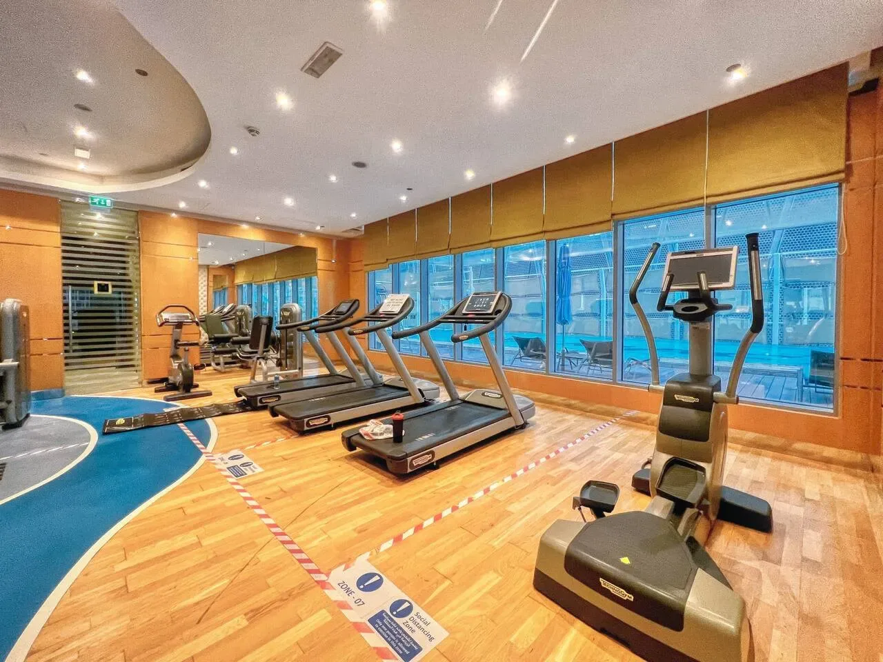 A gym with treadmills and exercise bikes beside large windows.