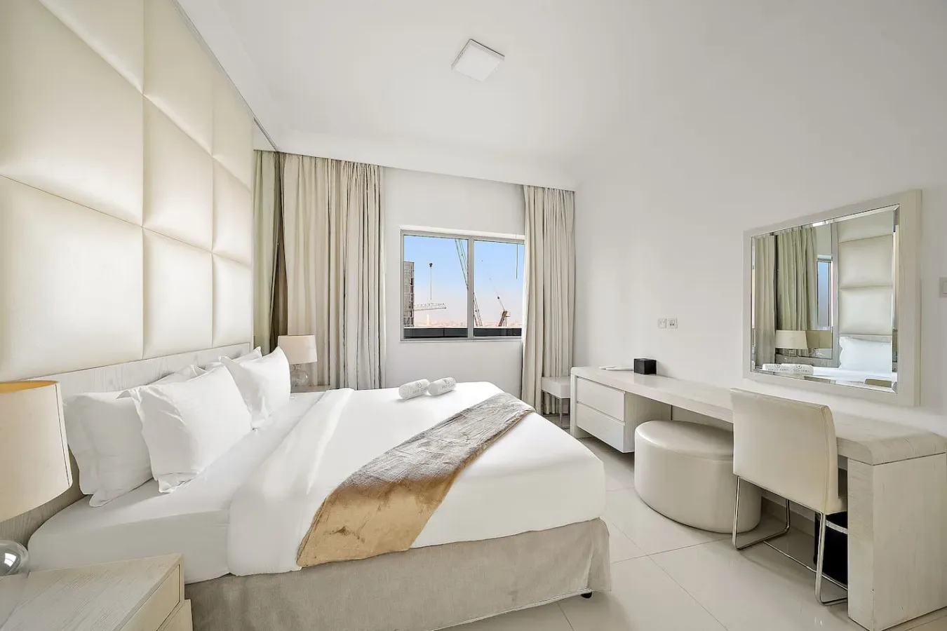 A bright bedroom with a bed, a window, and a desk with a mirror.