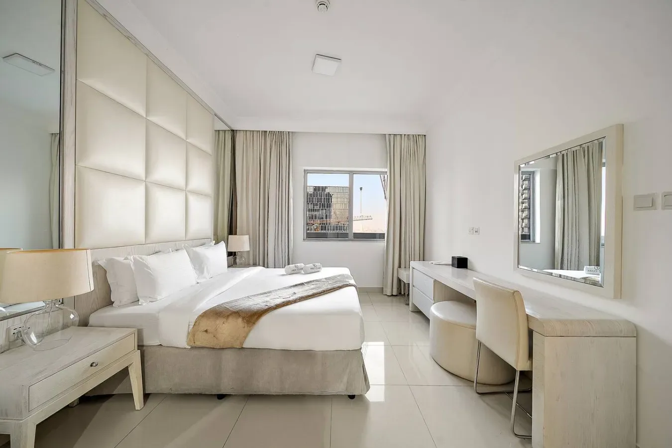 A bright bedroom with a bed, bedside tables, and a desk by the window.