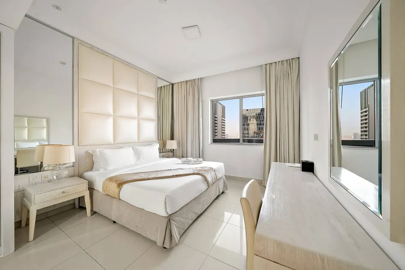 A bright bedroom with a neatly made bed, bedside tables, and a desk.