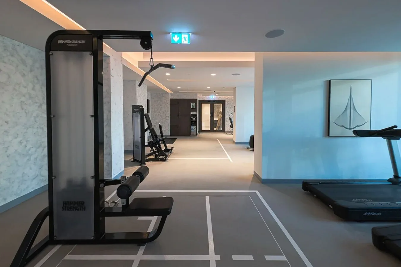 Un gimnasio con máquinas de ejercicio y una cinta junto a carriles marcados.