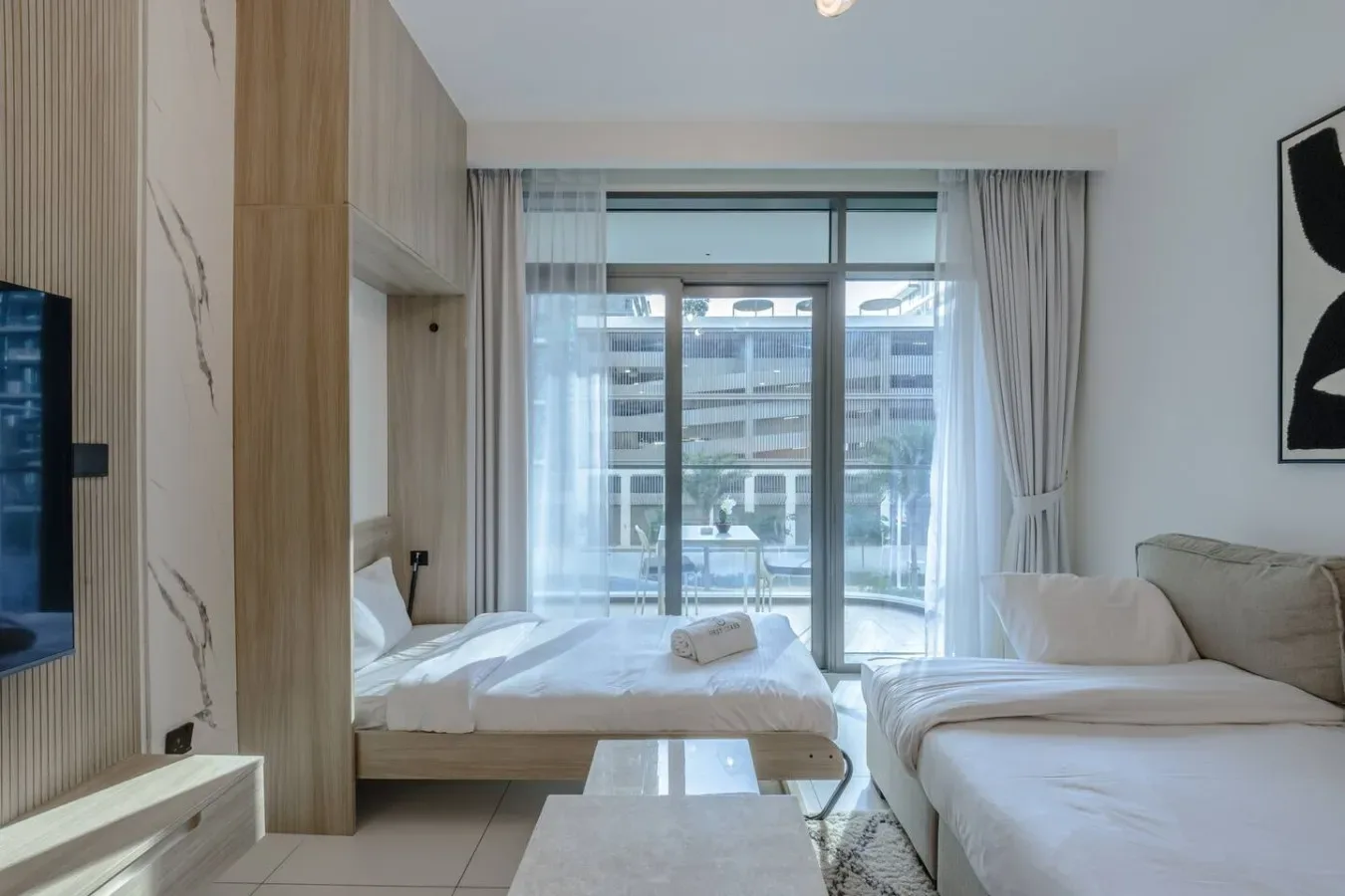 Dormitorio luminoso con zona de estar y una cama junto a una ventana grande.