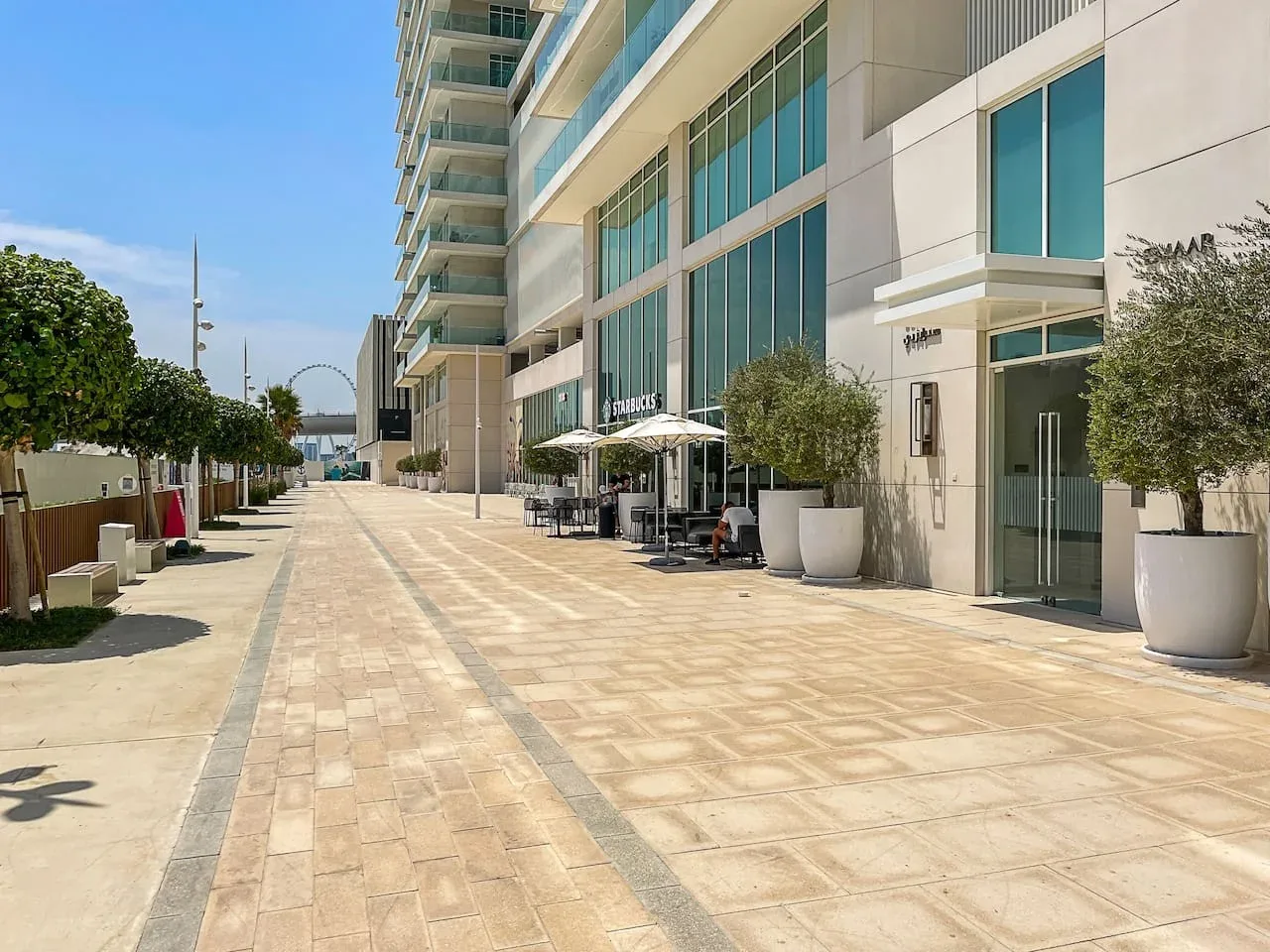 Un paseo peatonal pavimentado bordea un edificio moderno con asientos al aire libre.