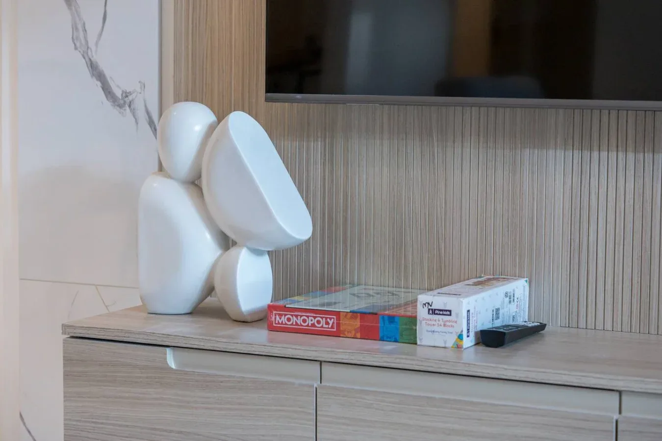 Una figura decorativa y juegos de mesa están sobre un mueble bajo una pantalla en la pared.