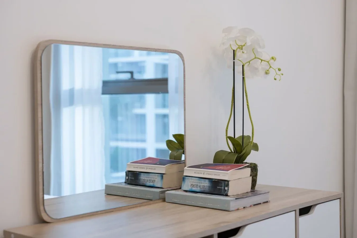 Una superficie con libros y una orquídea está frente a un espejo.