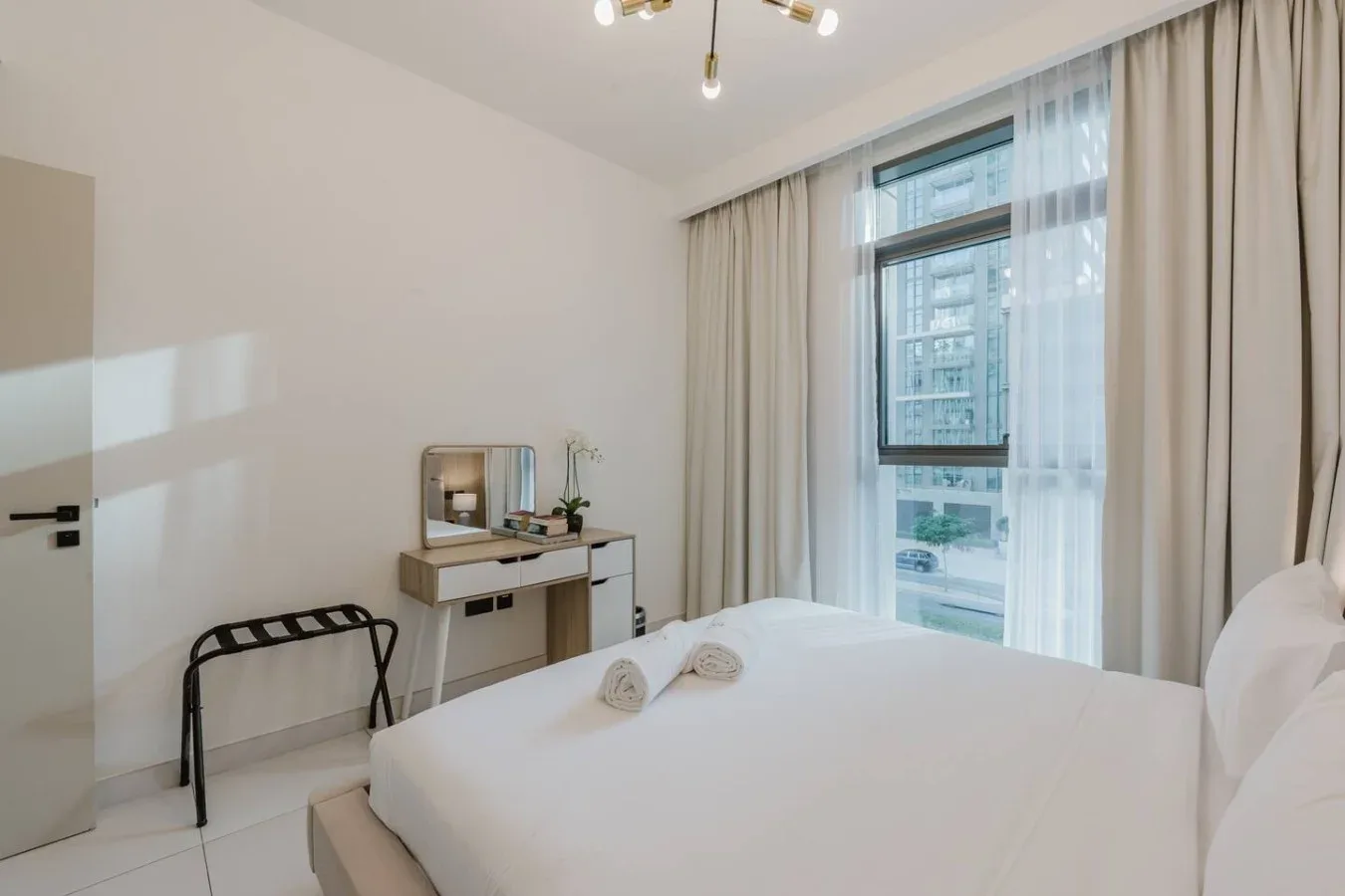 Un dormitorio luminoso con una cama bien hecha y un escritorio junto a la ventana.