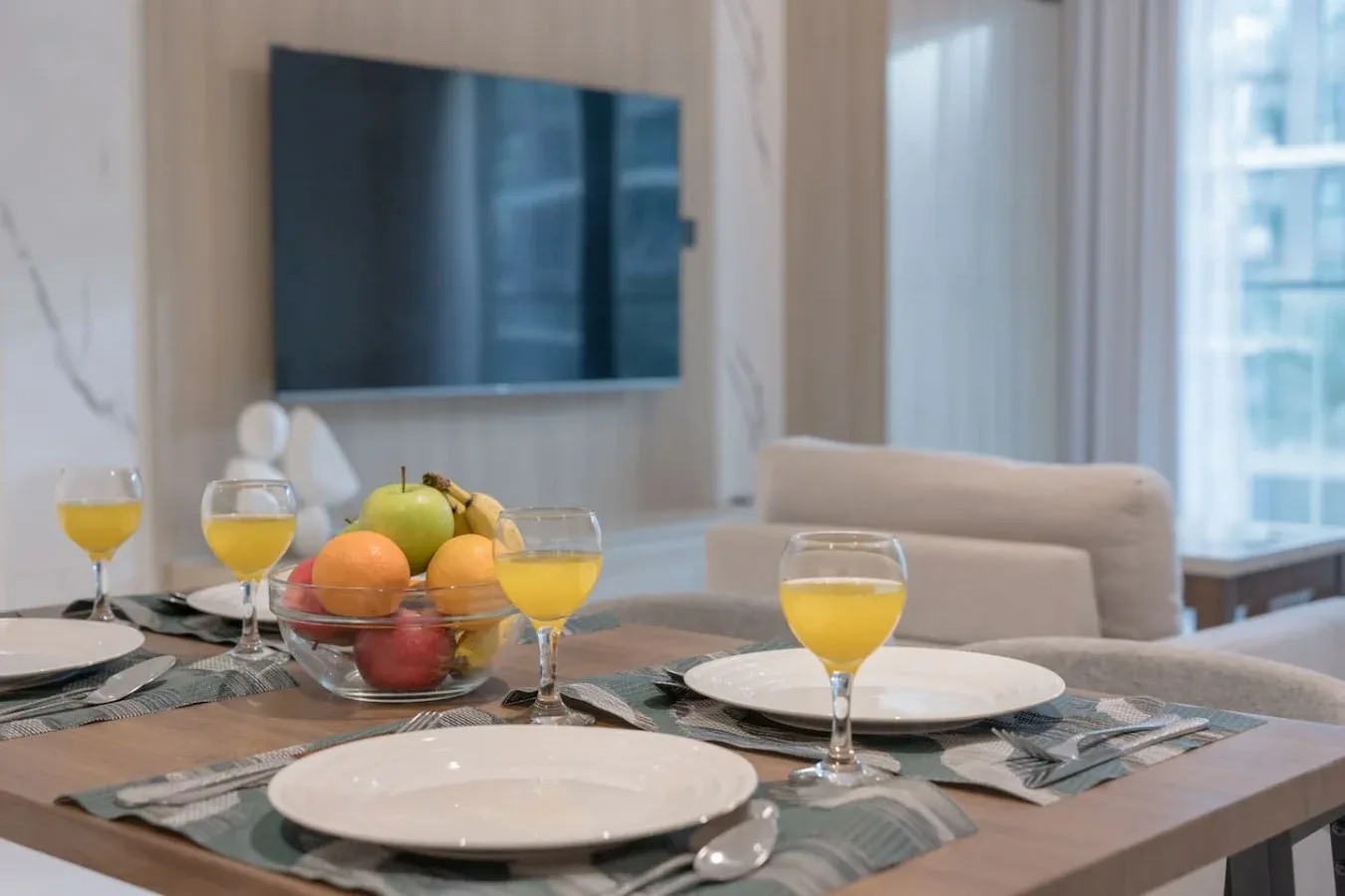 Una mesa de comedor puesta con platos, bebidas y fruta está frente a un televisor.