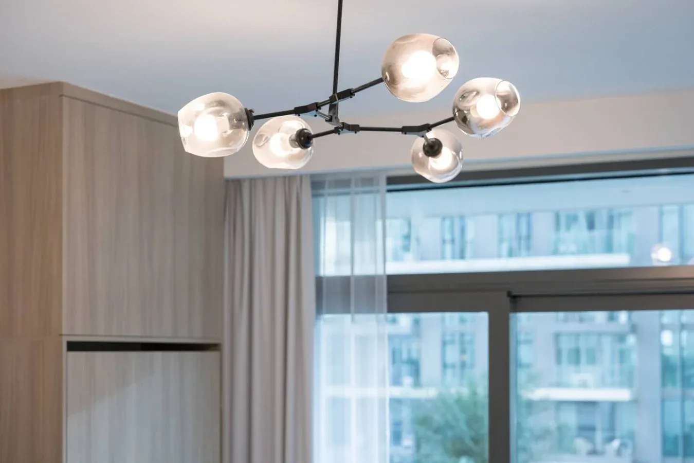 Una esquina de dormitorio con una lámpara colgante moderna, cortinas y una ventana grande.