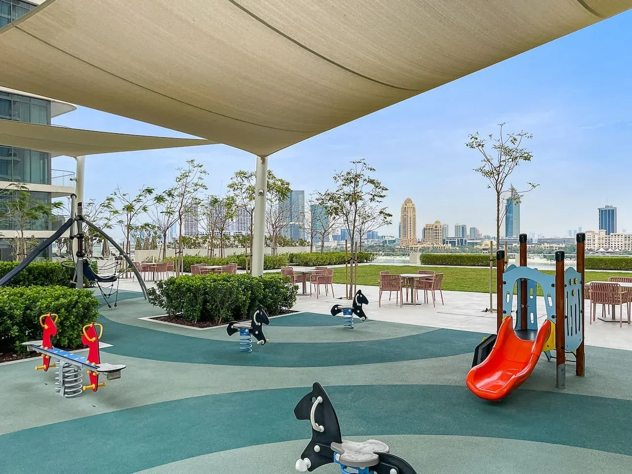 Un parque infantil al aire libre con toboganes y juegos está bajo una gran cubierta de sombra.