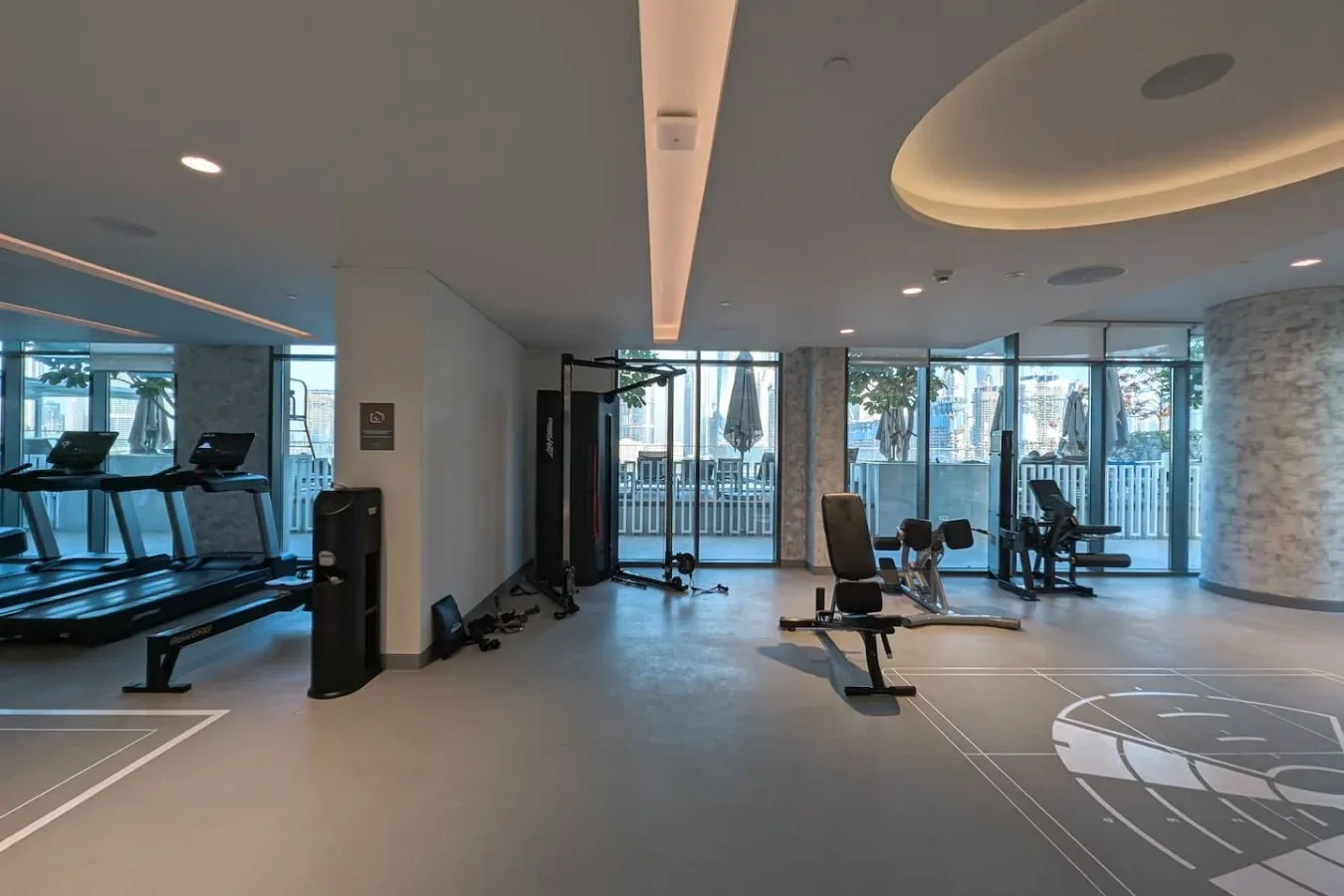 Una sala de ejercicio luminosa con equipos y grandes ventanales.