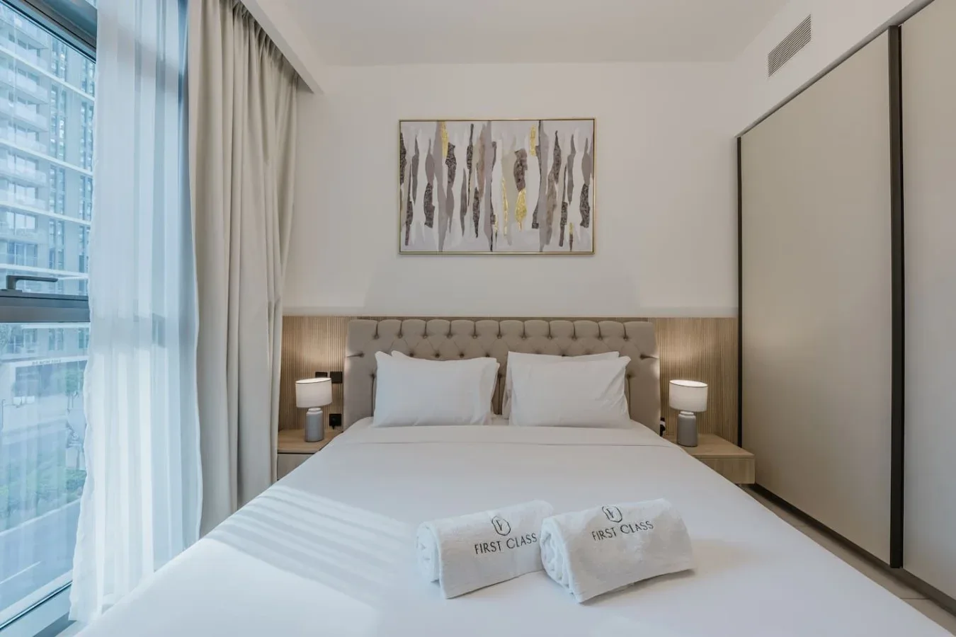 Un dormitorio luminoso con una cama bien tendida y un cuadro sobre el cabecero.