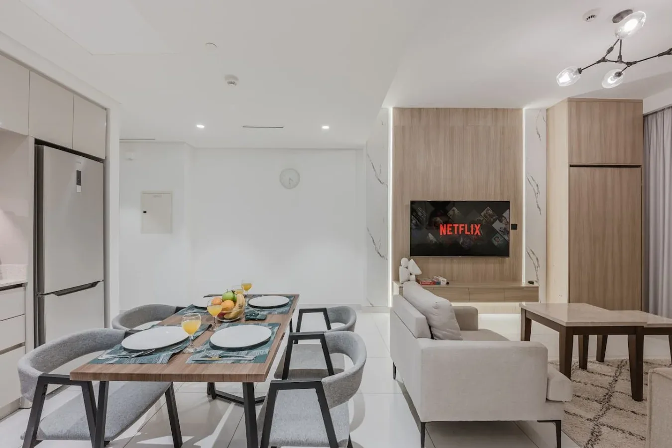 Comedor y sala de estar luminosos y abiertos, con un televisor en la pared del fondo.