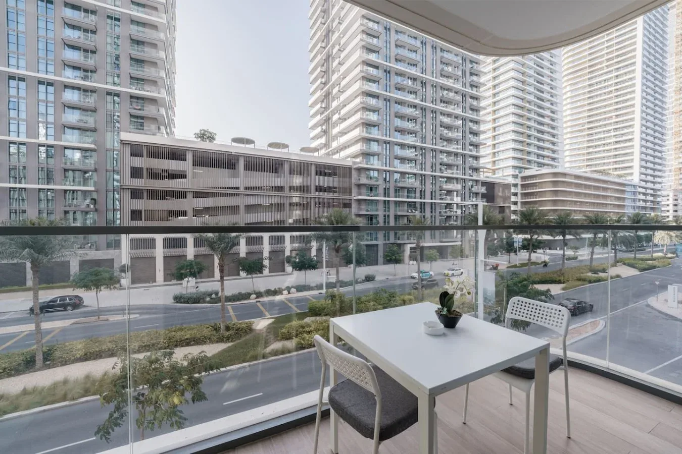 Un comedor en el balcón da a una calle ajardinada y edificios modernos de gran altura.