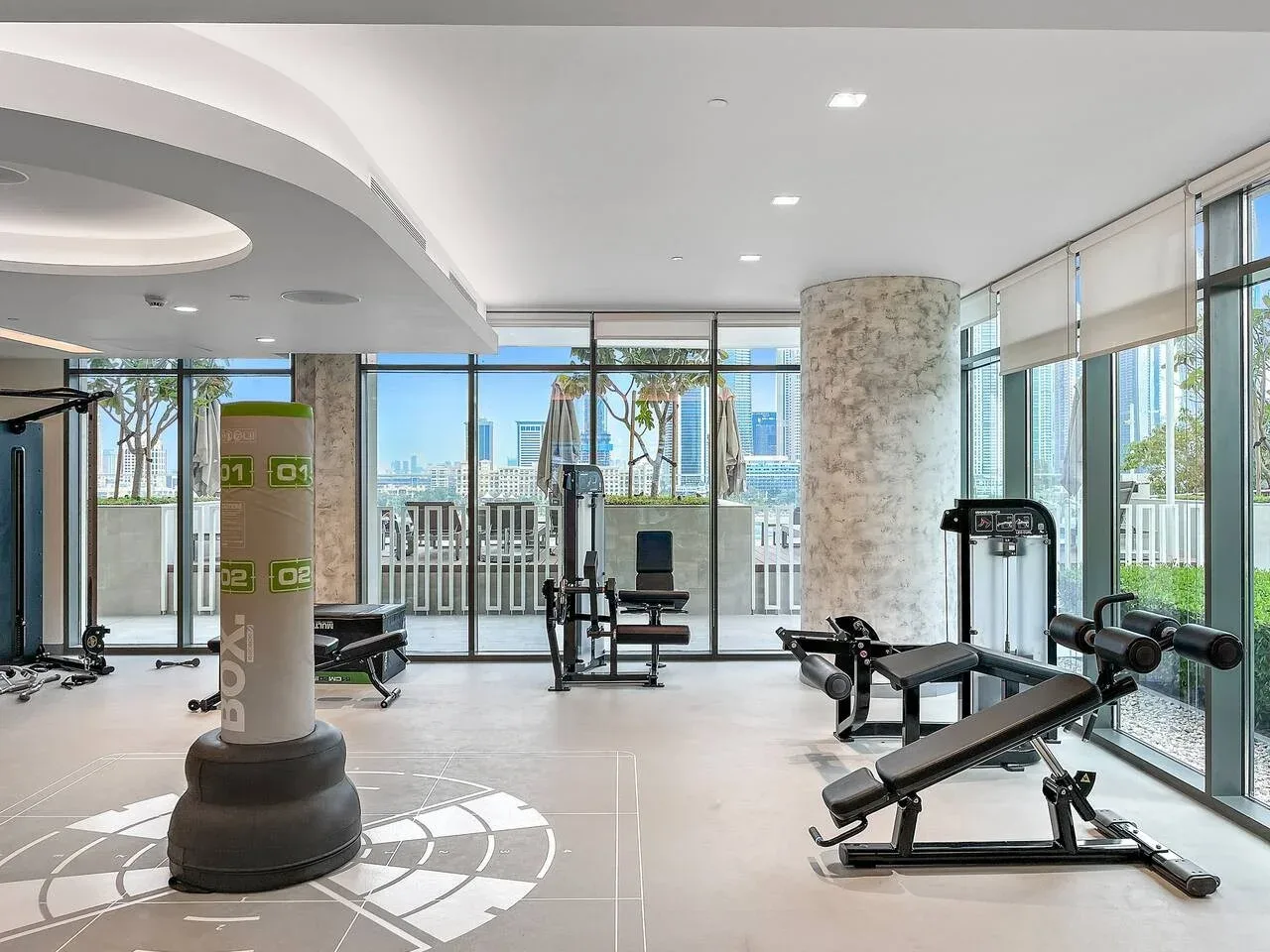 Un gimnasio luminoso con equipo de ejercicio junto a ventanas de piso a techo.
