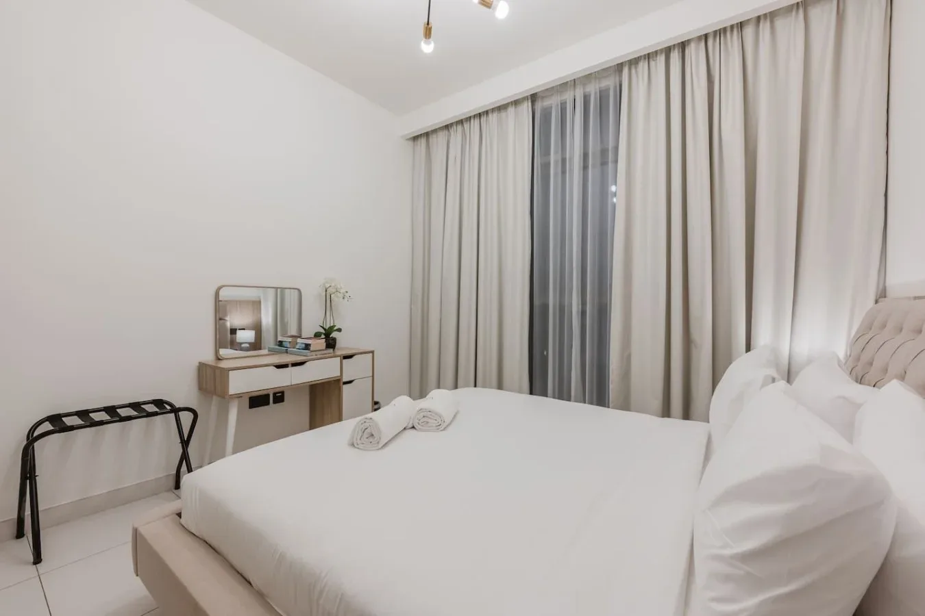 Un dormitorio luminoso con una cama ordenada y cortinas que cubren la ventana.