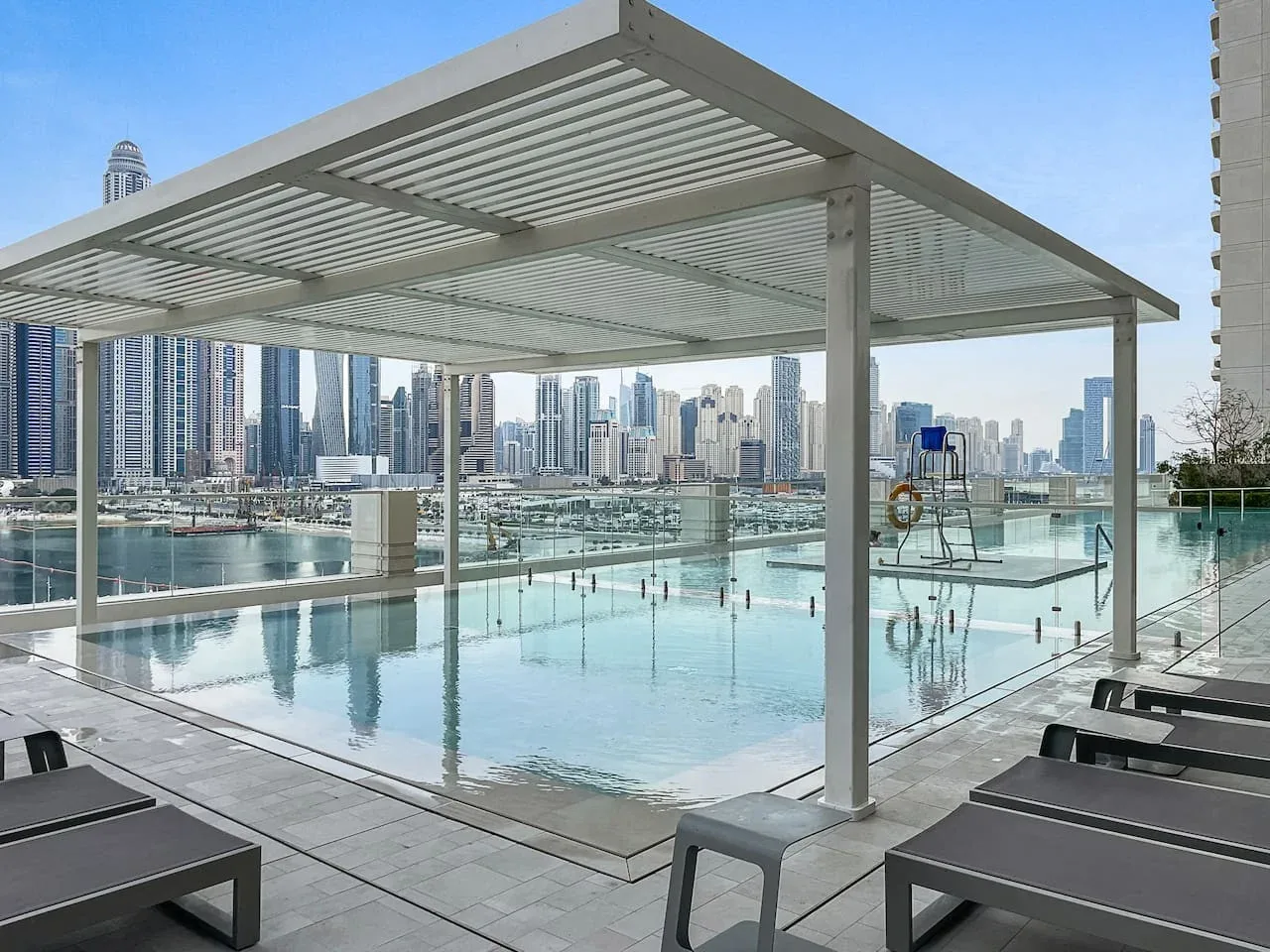 Una piscina en la azotea está bajo una pérgola, con edificios de la ciudad al fondo.