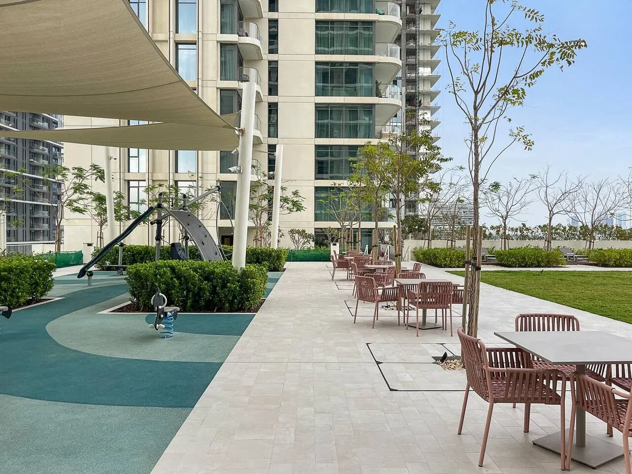 Una zona de asientos al aire libre junto a un pequeño parque infantil y edificios modernos.