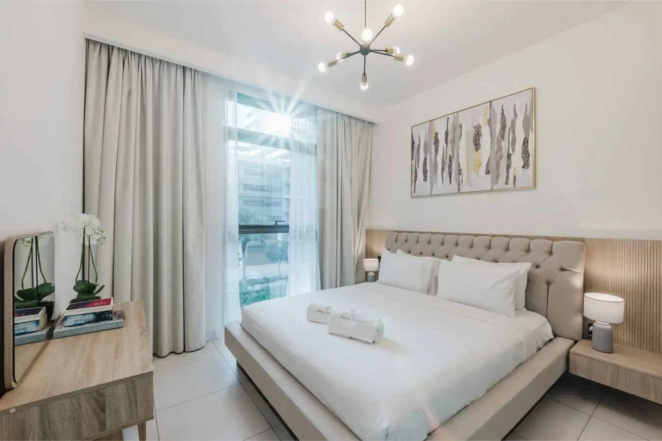 Un dormitorio con una cama bien tendida, cortinas claras y arte enmarcado.
