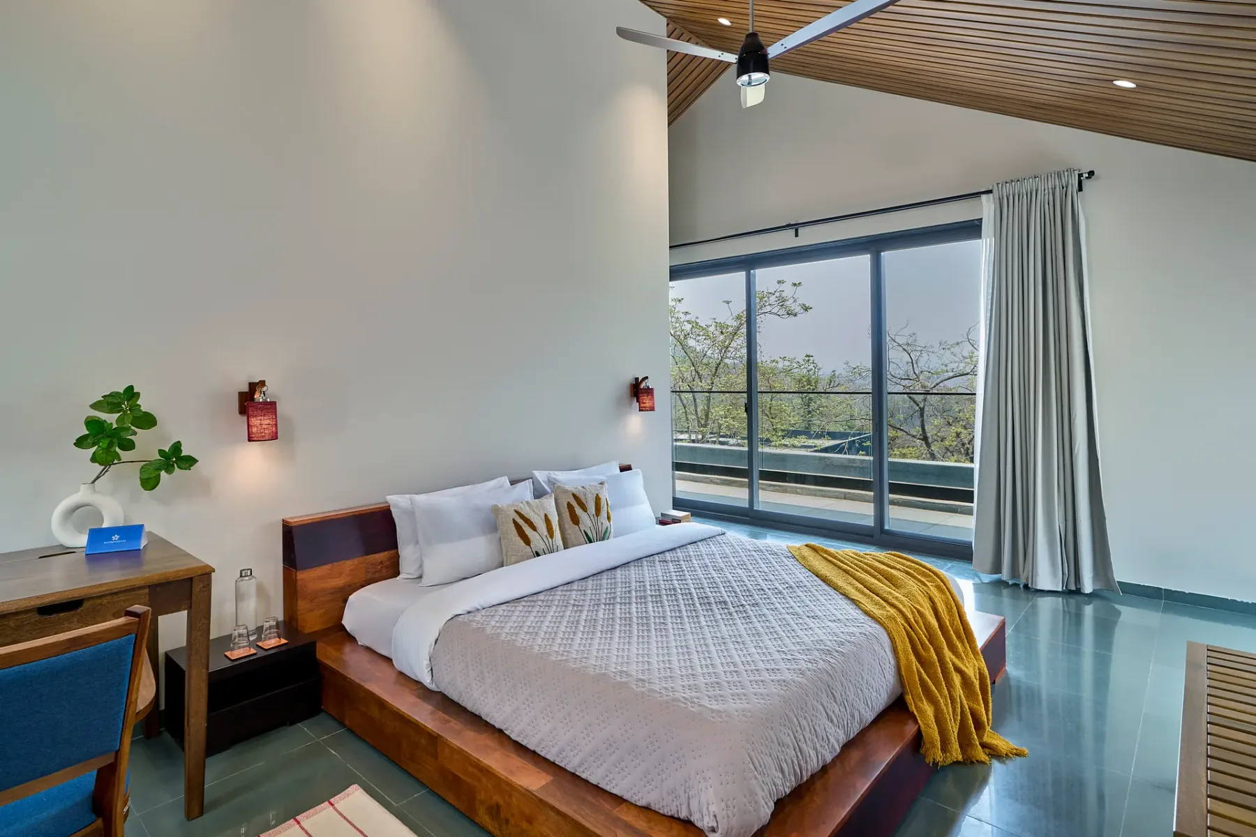 Dormitorio con una cama de madera junto a grandes ventanales y un balcón.