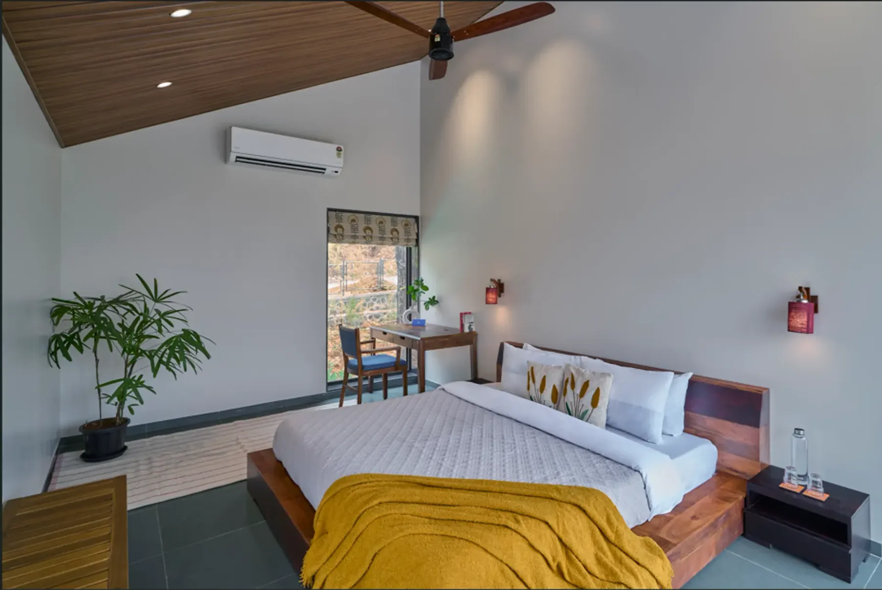 Dormitorio con una cama de madera, ropa de cama blanca y una manta color mostaza.