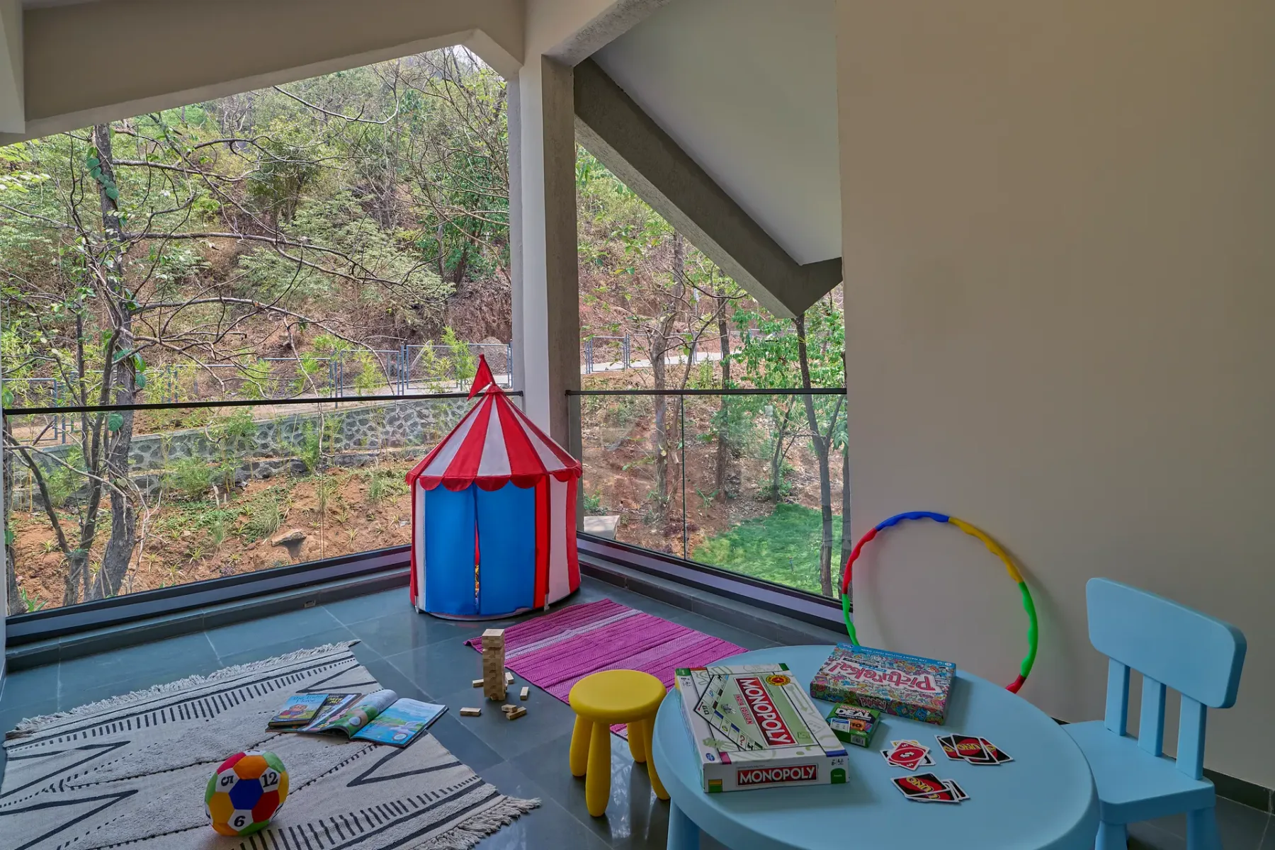 Una zona de juegos con una pequeña tienda colorida y juguetes junto a ventanas de vidrio.