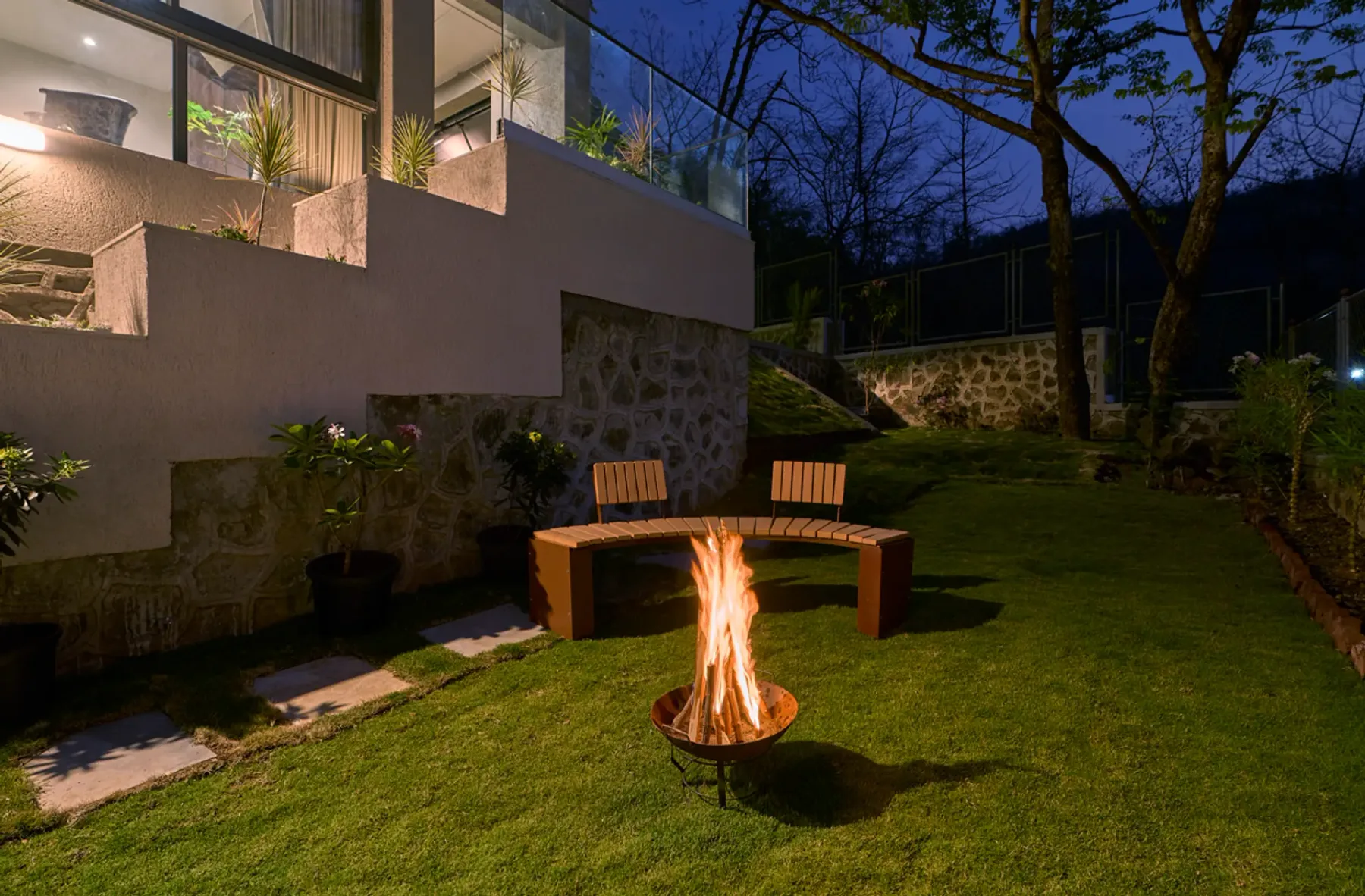 Un jardín al anochecer con un banco curvo alrededor de un brasero.