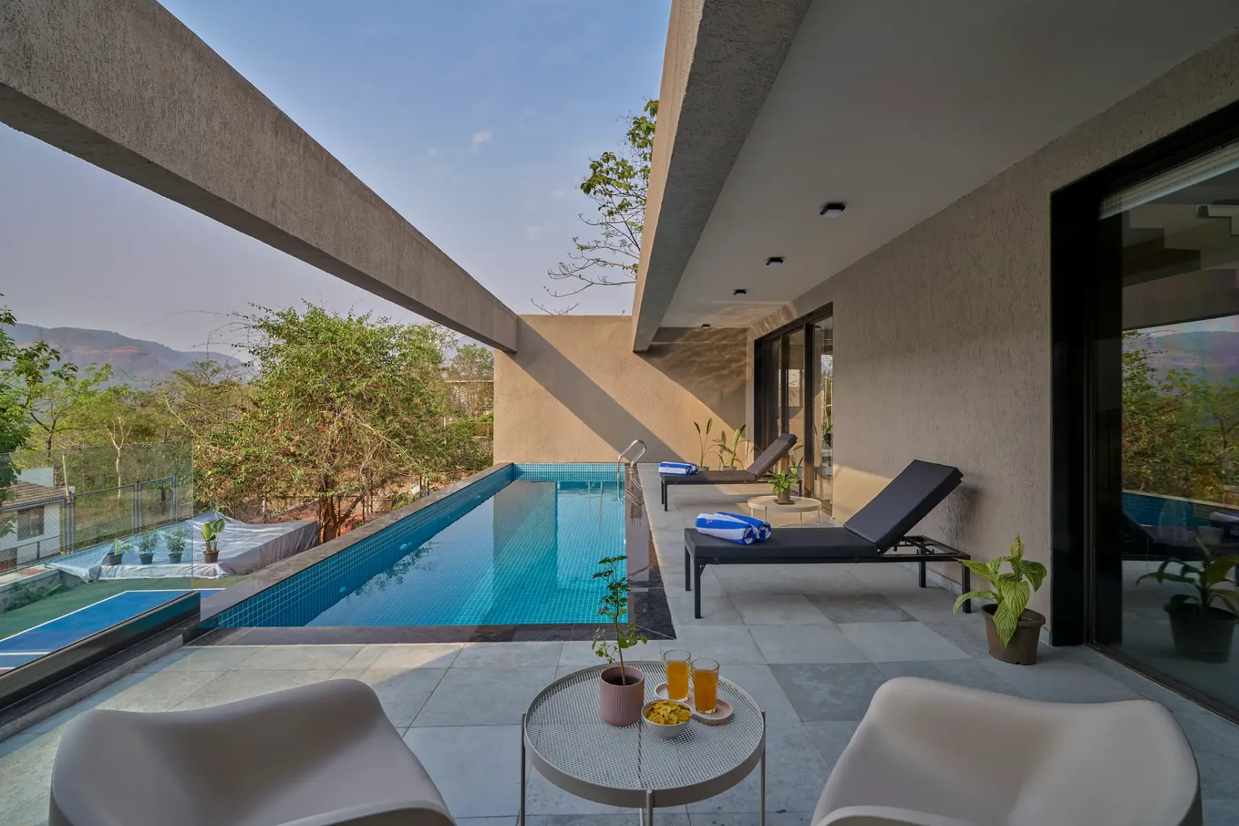 Un patio moderno junto a una piscina, con asientos y una mesa.