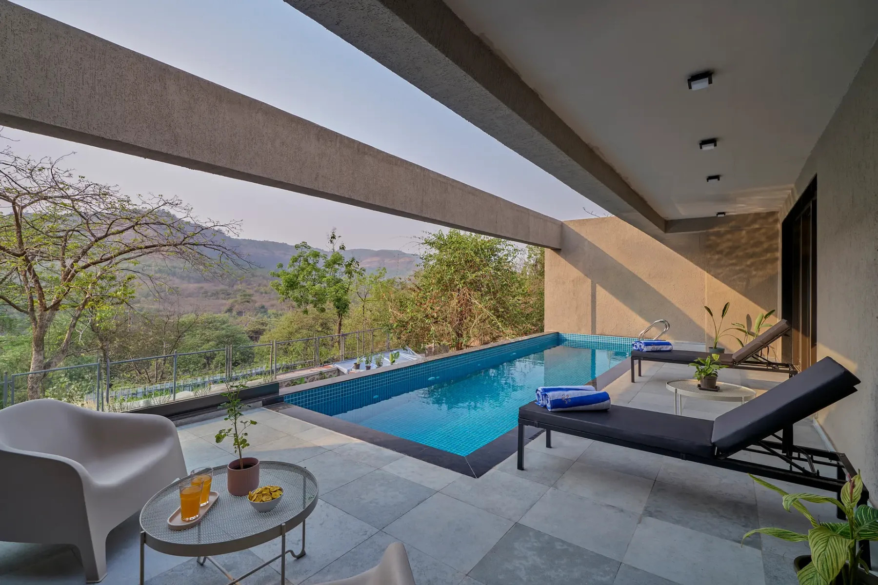Una terraza exterior moderna junto a una piscina, con asientos de descanso y vistas a las montañas.
