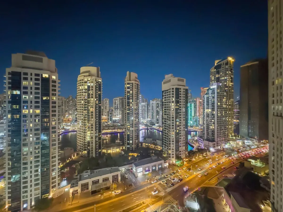 Un horizonte urbano nocturno con edificios altos iluminados y calles transitadas.