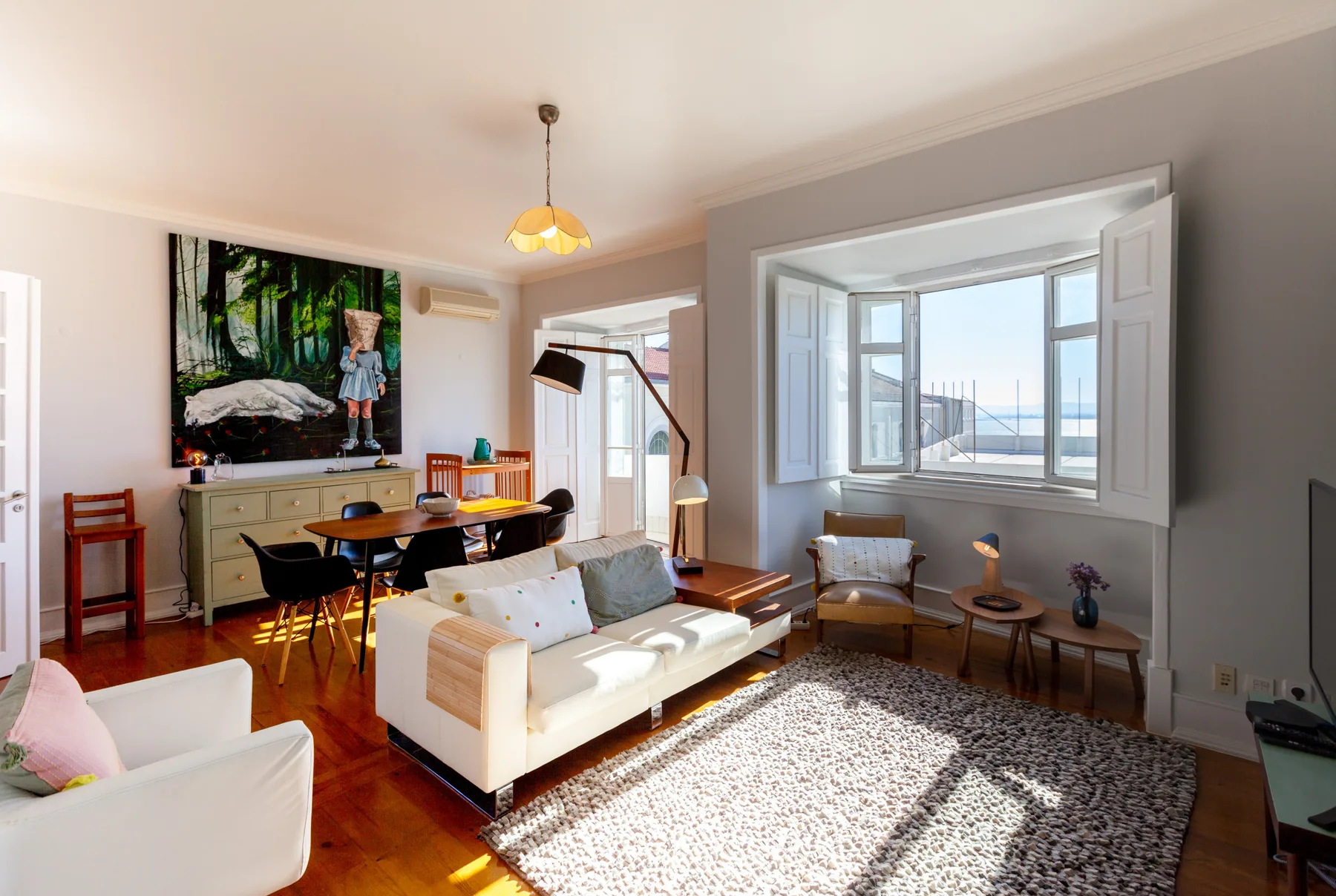 A bright living room with seating around a dining table beside a large window.