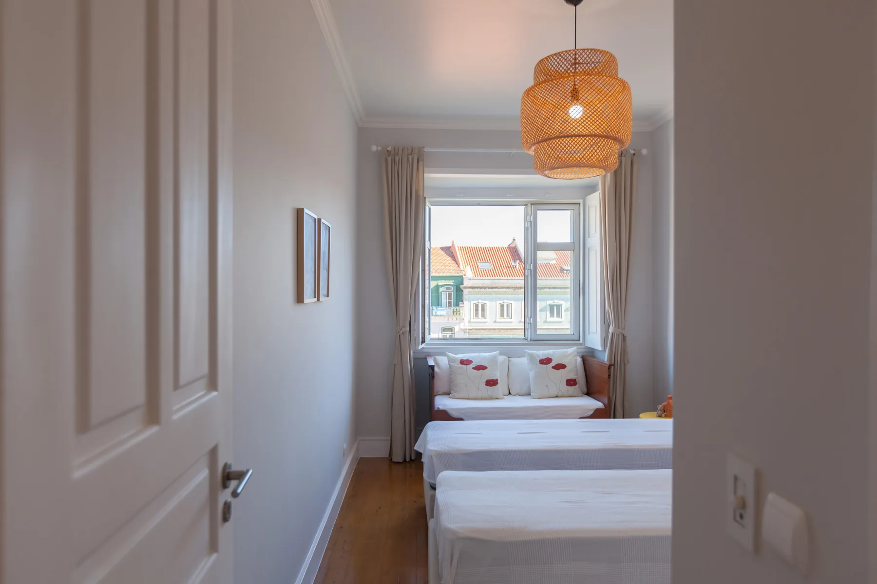 A narrow bedroom has two beds beneath a large window.